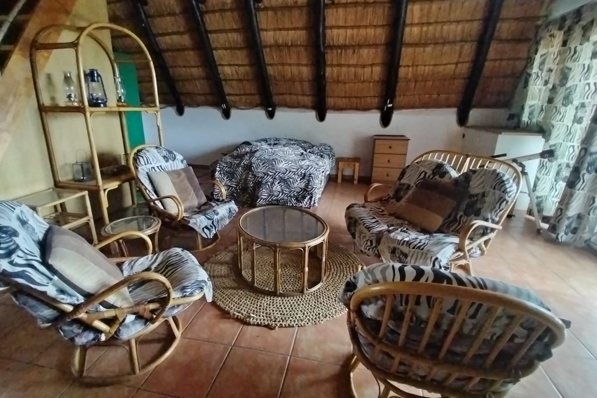A rustic living area featuring a traditional thatched roof with exposed timber rafters and ceramic tiled flooring.