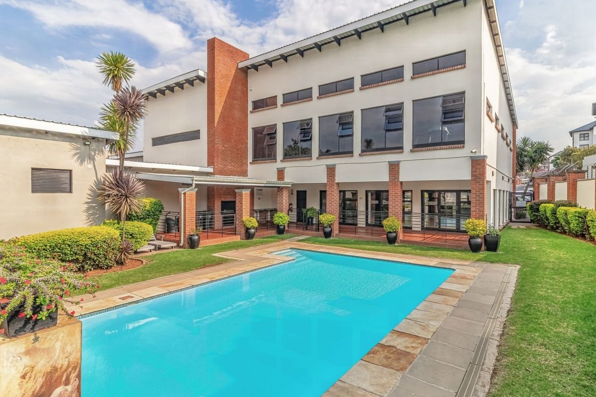 Rear exterior view of the property featuring a well-maintained swimming pool, stone-paved pool deck, covered patio area, and landscaped garden.