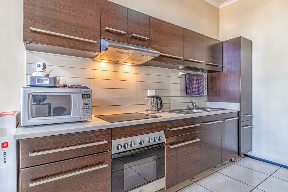 A functional kitchen featuring dark wood-finish cabinetry, integrated appliances including an oven and hob, tiled backsplash, and durable floor tiling.