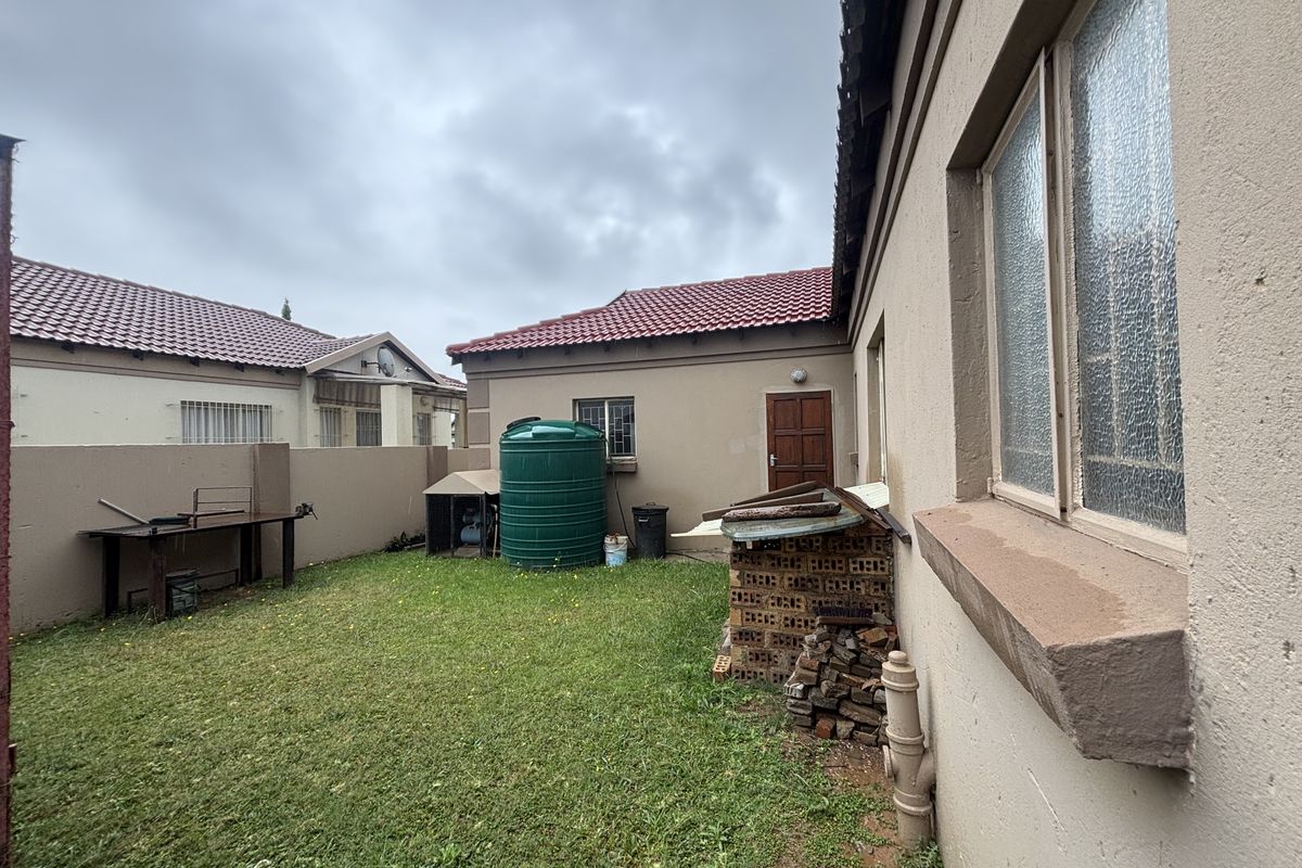 Rear exterior view of the townhouse featuring a small lawn, perimeter wall, and a water storage tank.