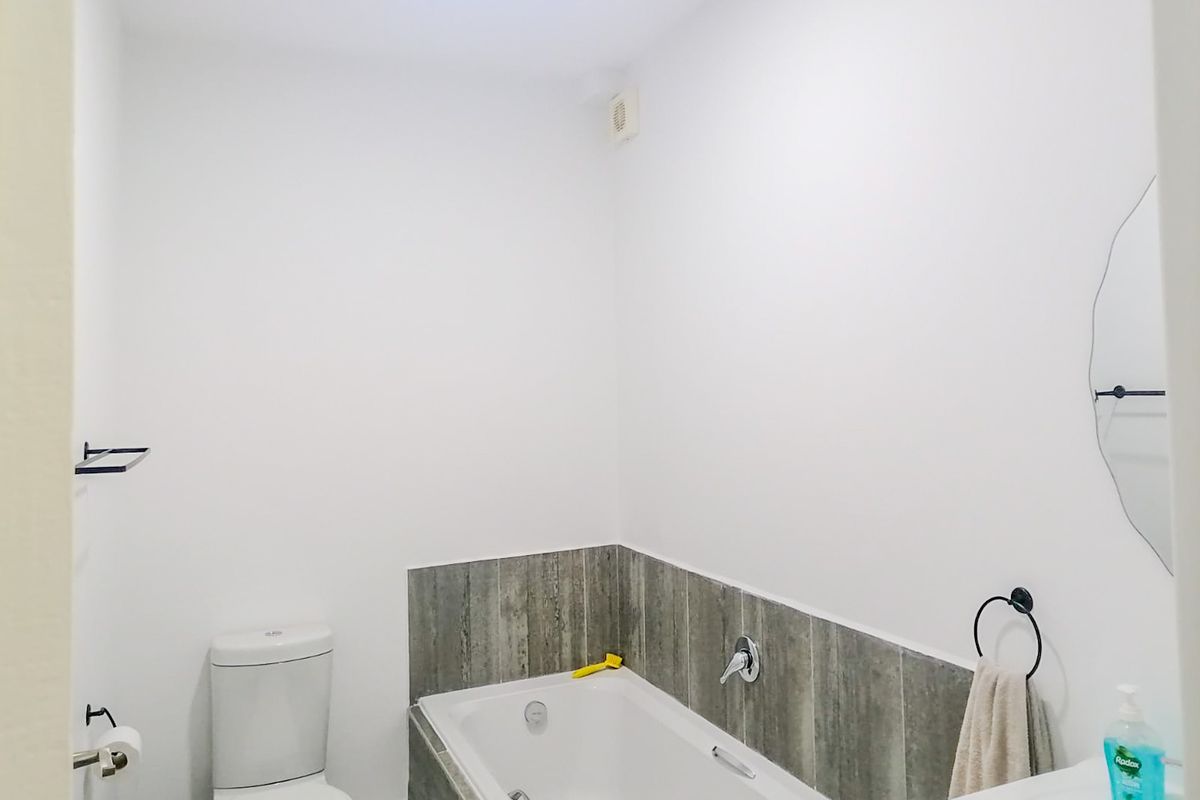 A clean, functional bathroom featuring a built-in bathtub with tiled surround, a standard toilet, and a wall-mounted basin.
