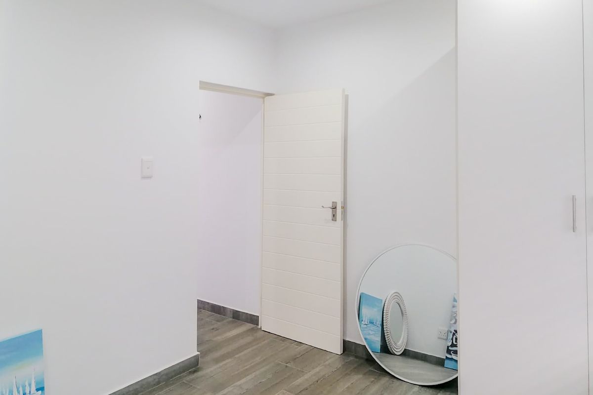 A bright, minimalist bedroom featuring neutral tiled flooring, recessed downlighting, and a built-in wardrobe, offering a clean and modern blank canvas.