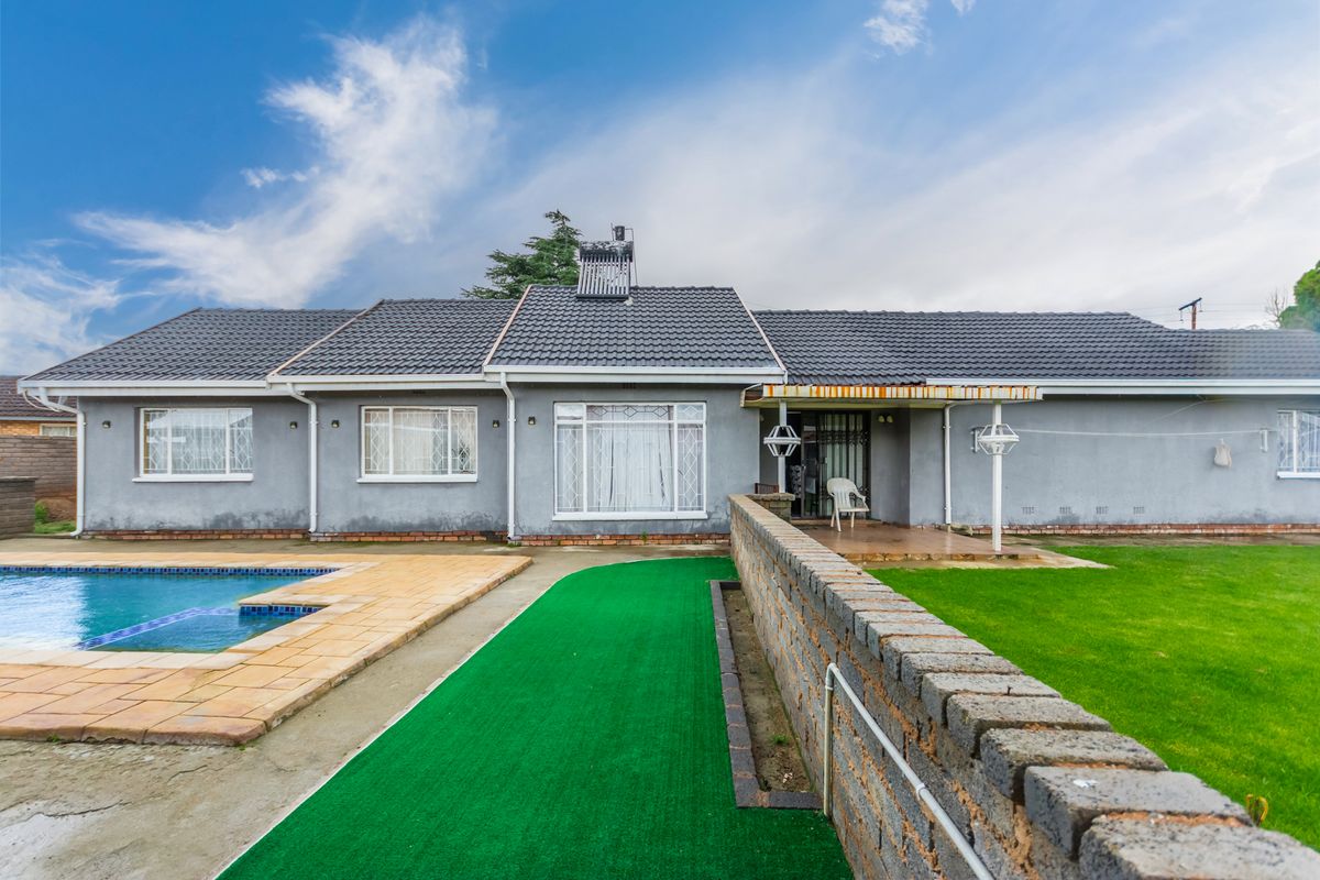 Rear view of the property featuring a swimming pool, paved patio area, and a well-maintained garden with a brick boundary wall.