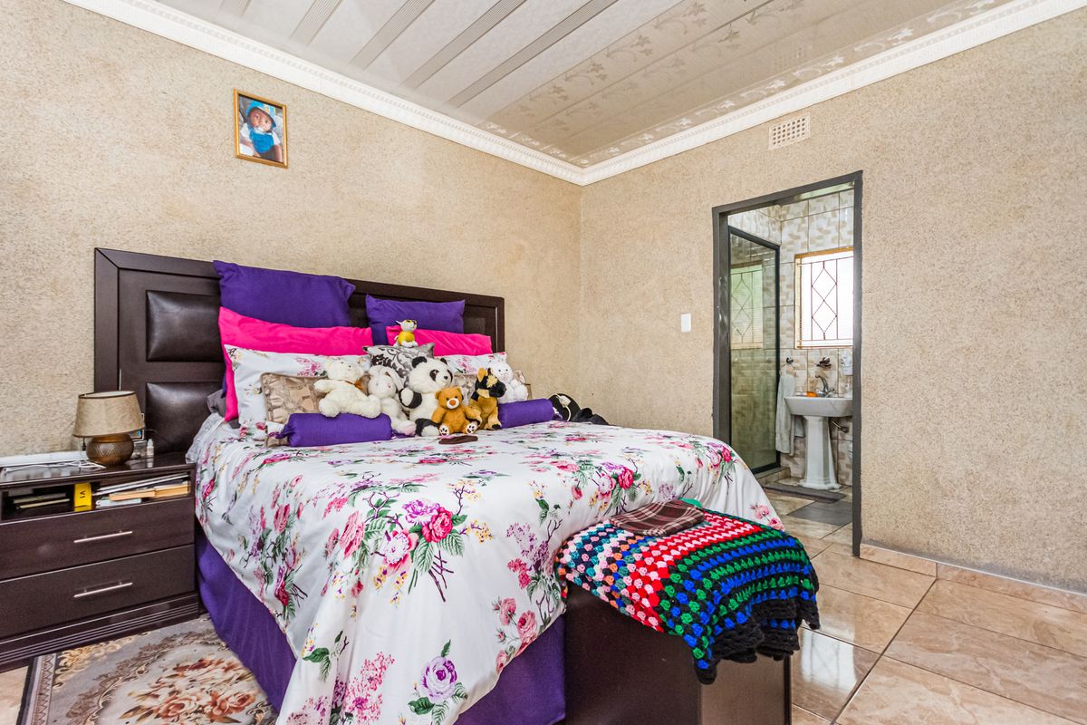 A bedroom featuring tiled flooring, textured wall finishes, and an en-suite bathroom with a pedestal basin and shower enclosure.
