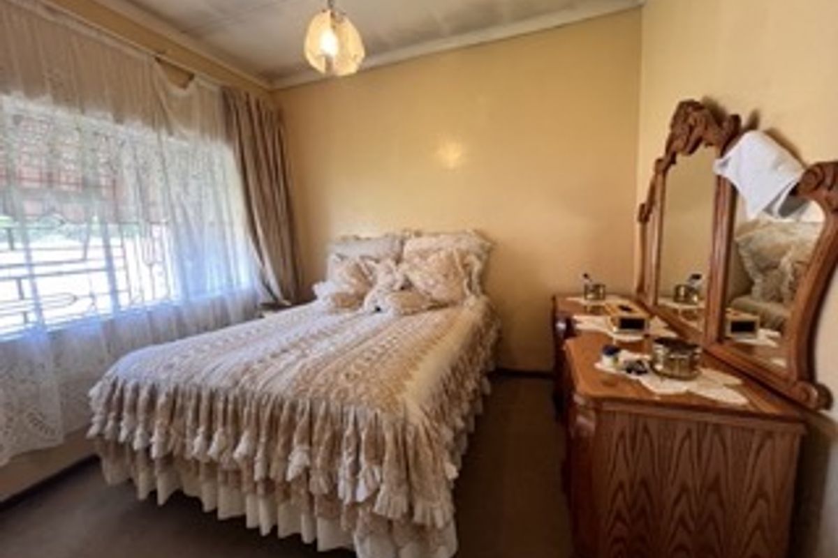 A bedroom featuring a large window with security bars, carpeted flooring, and a central ceiling light fixture.