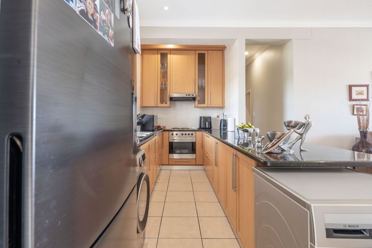 A functional kitchen featuring light wood cabinetry, granite countertops, and integrated stainless steel appliances, with a breakfast bar overlooking the living area.