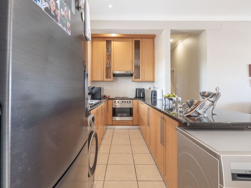 A functional kitchen featuring light wood cabinetry, granite countertops, and integrated stainless steel appliances, with a breakfast bar overlooking the living area.