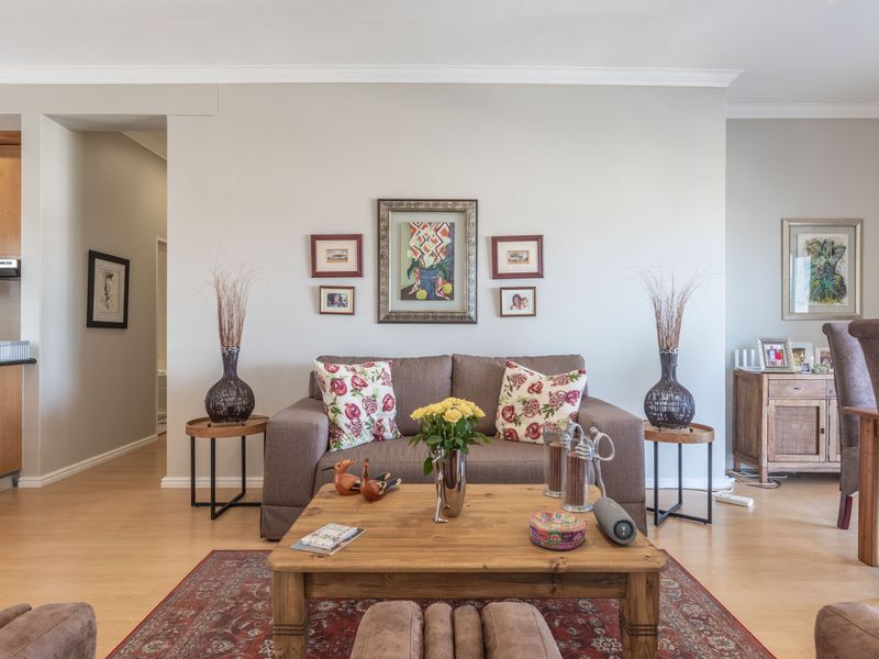 An open-plan living and dining area featuring laminate flooring, coving, and a functional kitchen with built-in cabinetry and granite countertops.