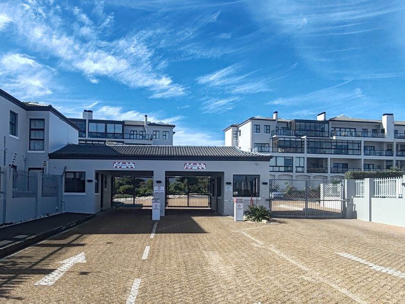 A secure gated entrance to an apartment complex featuring a guard house, paved driveway, and perimeter security fencing.