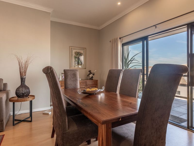 Open plan living and dining area featuring laminate flooring, crown molding, and large sliding glass doors leading to a balcony.