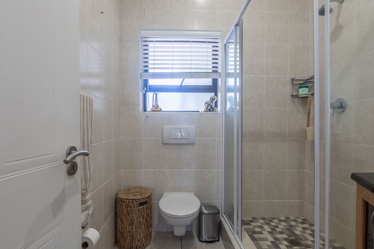 A compact, well-maintained bathroom featuring a wall-mounted toilet, a glass-enclosed shower, and neutral wall tiling.