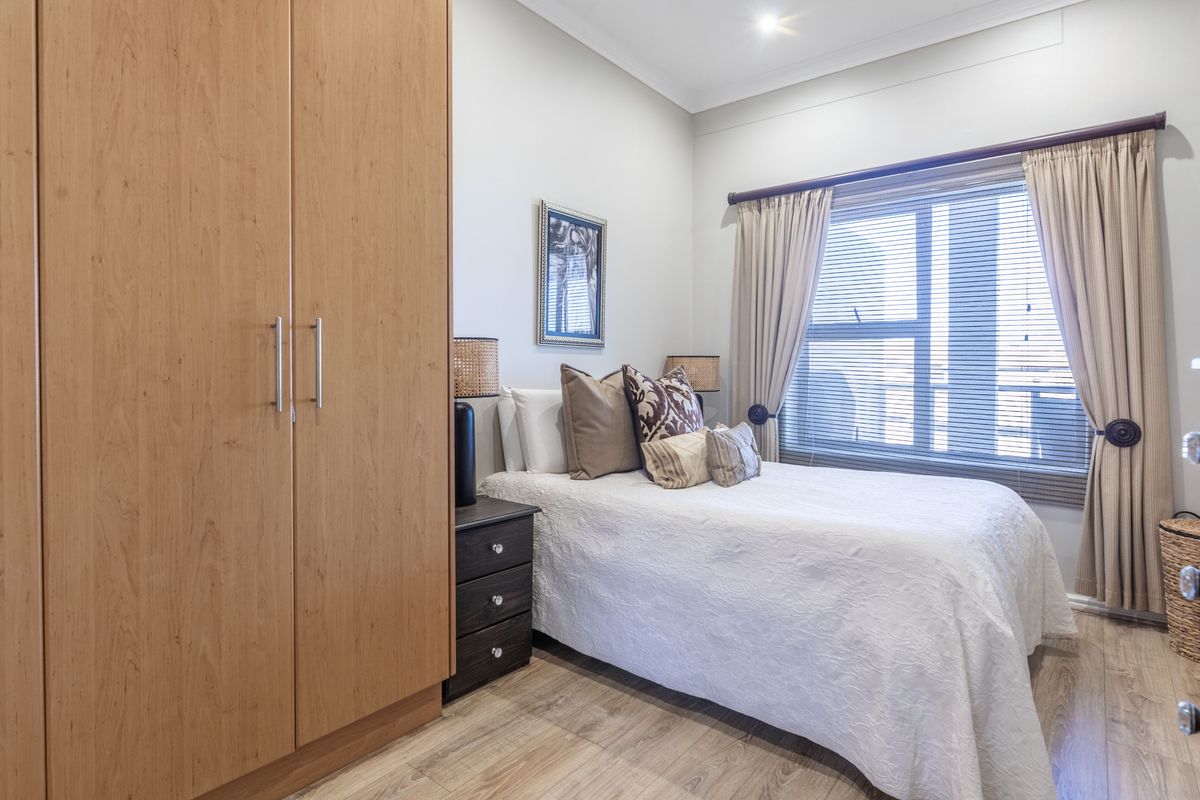 A well-maintained bedroom featuring light-toned laminate flooring, a large built-in wardrobe, and window treatments including blinds and curtains.