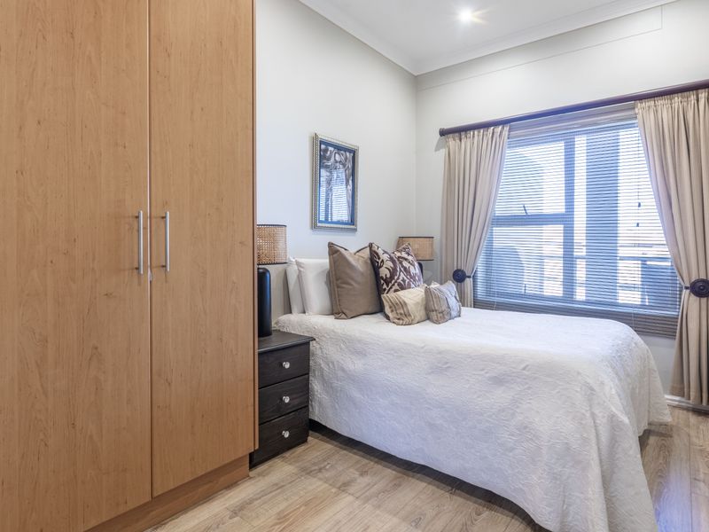 A well-maintained bedroom featuring light-toned laminate flooring, a large built-in wardrobe, and window treatments including blinds and curtains.