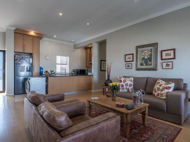 An open-plan living area featuring a functional kitchen with built-in cabinetry and a comfortable lounge space with laminate flooring and recessed lighting.