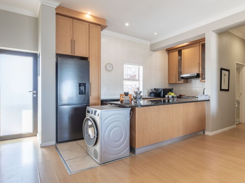 Open-plan kitchen featuring light wood cabinetry, granite countertops, and an integrated extractor fan, seamlessly flowing into the living area with laminate flooring.
