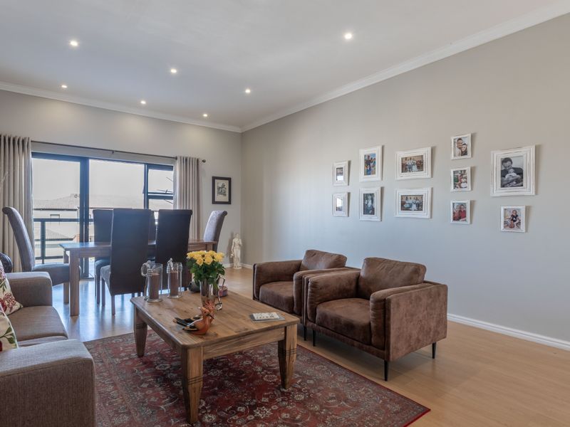 Spacious open-plan living and dining area featuring laminate flooring, recessed downlighting, and large sliding glass doors leading to an outdoor balcony.