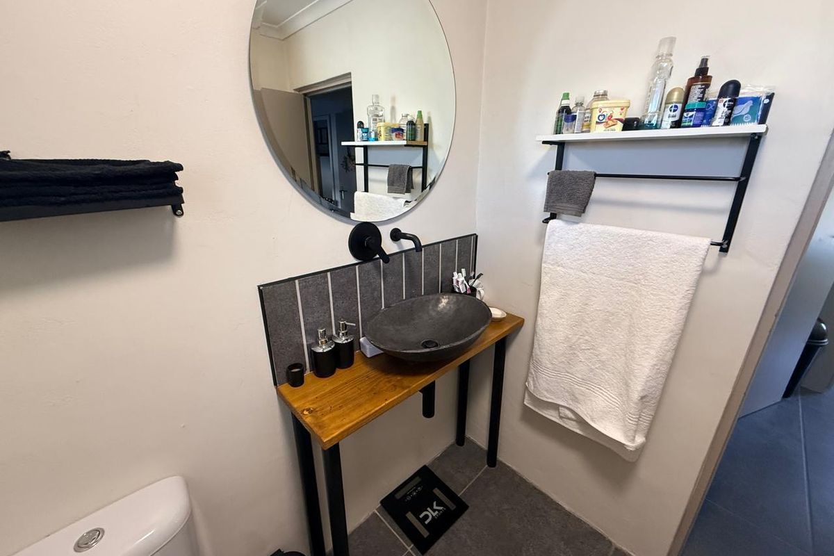 A modern bathroom featuring a vessel sink on a wooden vanity, a circular wall mirror, and tiled splashback with matte black fixtures.