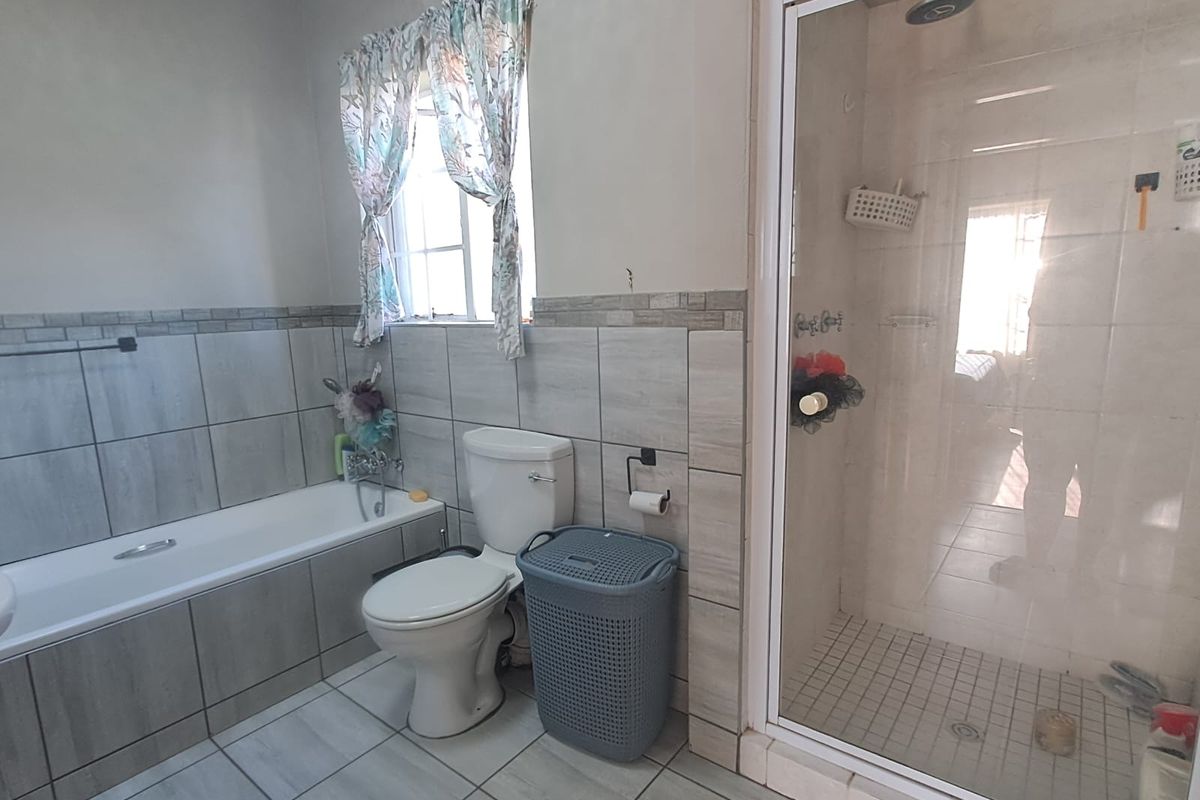 A functional bathroom featuring a built-in bathtub, a separate glass-enclosed shower, and neutral tiled finishes throughout.
