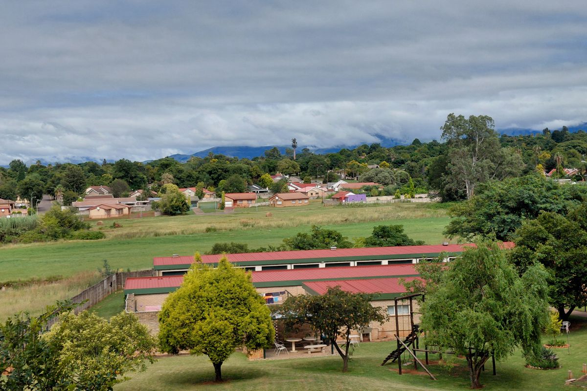 An elevated aerial view of a residential complex featuring red metal roofs, surrounding green lawns, and a scenic backdrop of trees and mountains.
