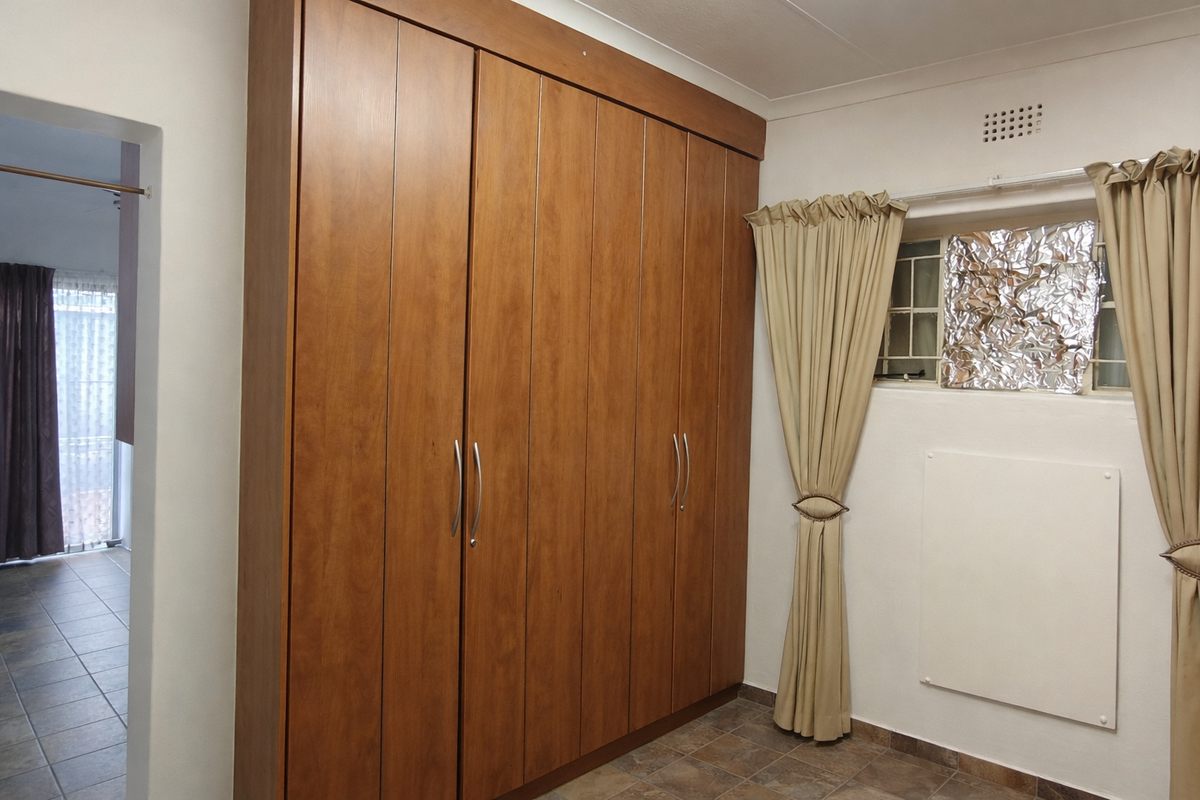 A bedroom featuring a large built-in wooden wardrobe, tiled flooring, and a window with a ventilation grille.