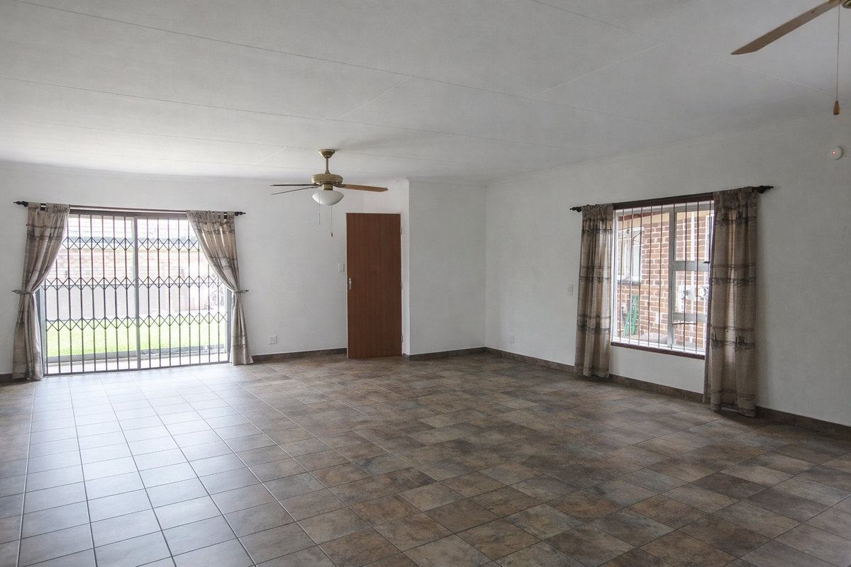 Spacious, light-filled living area featuring neutral tiled flooring, ceiling fans, and secure access to the exterior.