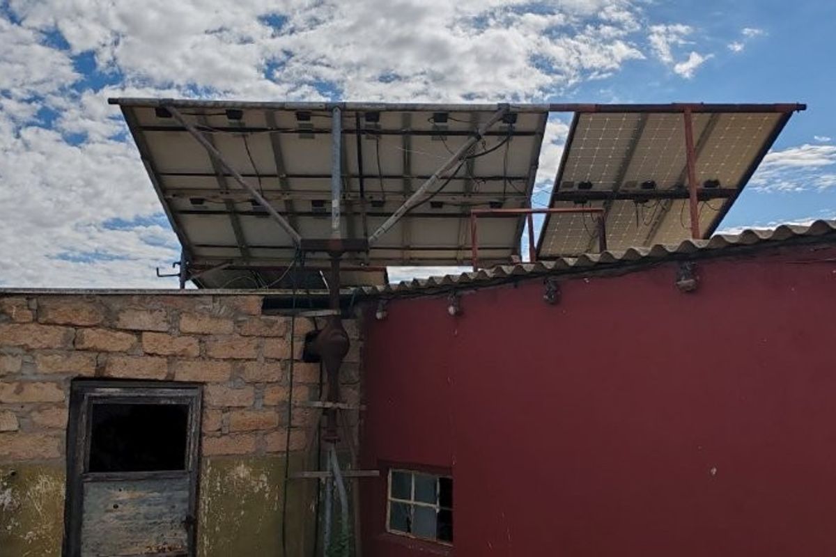 Exterior view of a farm building featuring mounted solar panels, stone and plastered wall construction, and visible signs of weathering and maintenance requirements.