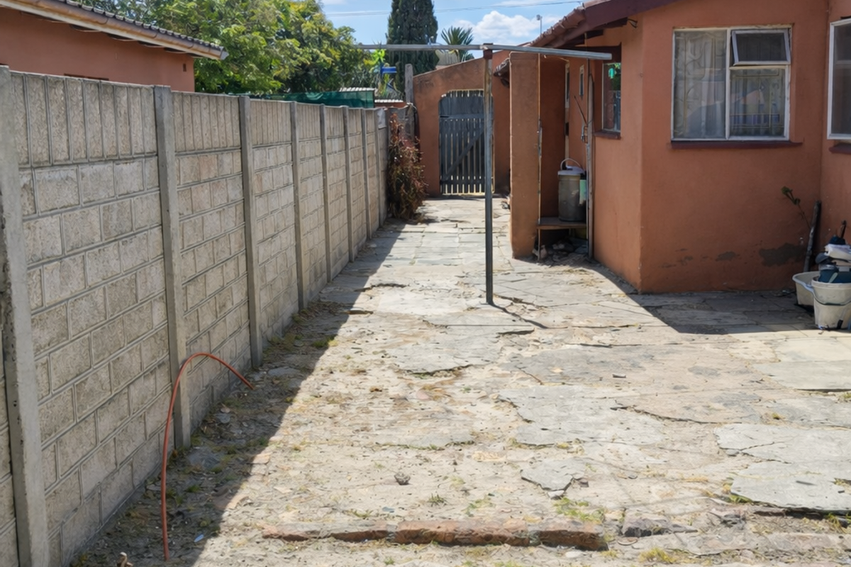 A side exterior area featuring a concrete block boundary wall, paved ground surface, and access to the rear of the property.