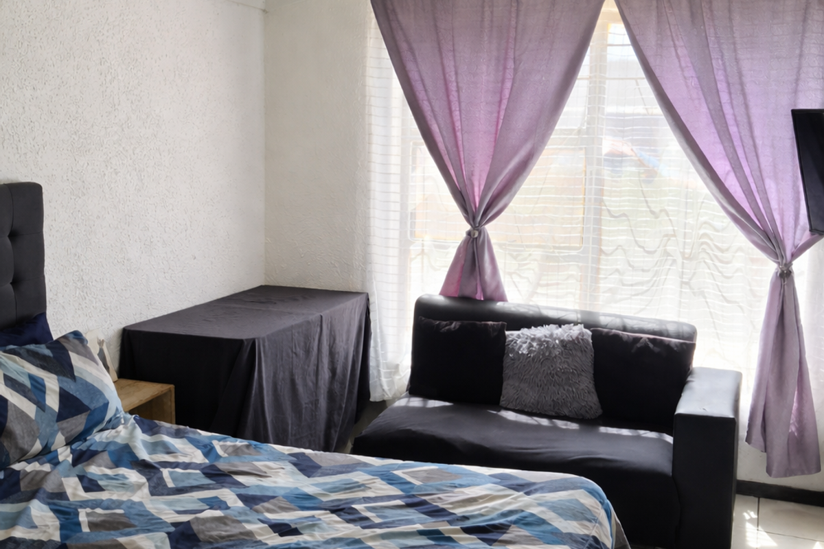 A bedroom featuring tiled flooring, a sloped ceiling with exposed beams, and large windows with curtains.
