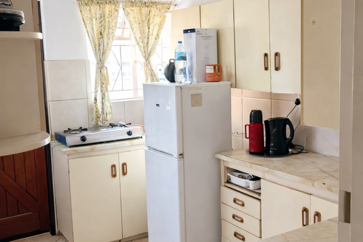 A functional kitchen featuring dated cabinetry, tiled flooring, and built-in stove top, offering a practical layout with potential for modernization.