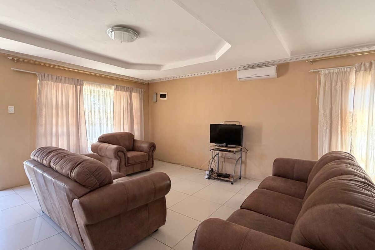 A spacious living room featuring tiled flooring, a coved ceiling, and a wall-mounted split-system air conditioner.