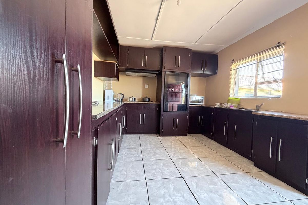 A functional kitchen featuring dark wood cabinetry, laminate countertops, built-in oven, extractor fan, and tiled flooring with a window for natural light.