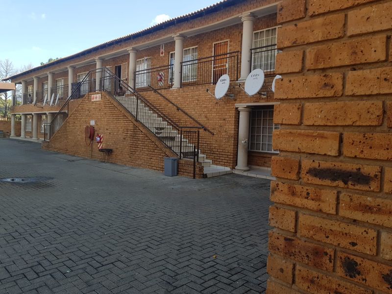 Exterior view of a multi-story brick apartment complex featuring an external staircase, paved driveway, and balcony access.