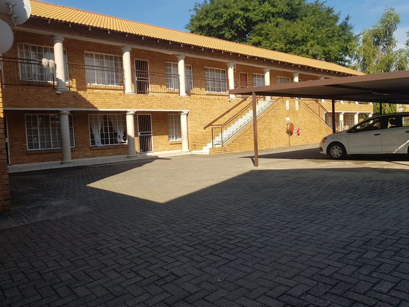 Exterior view of a two-story facebrick apartment complex featuring a paved parking area, covered carport, and external staircase access to upper units.