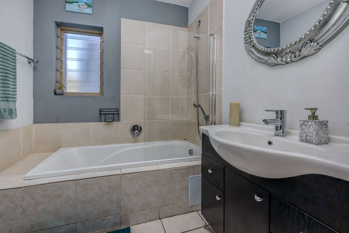 A functional bathroom featuring a built-in bathtub with a glass screen, a vanity cabinet with a basin, and tiled finishes.