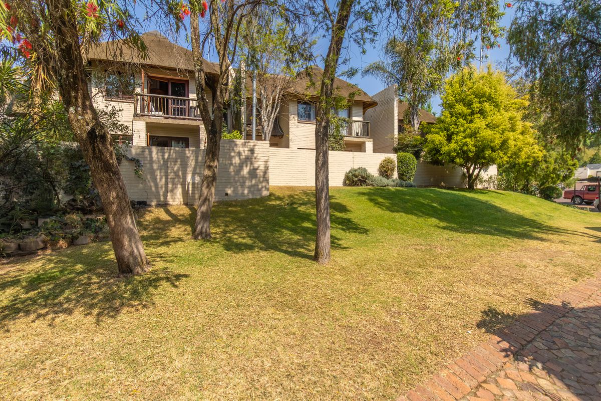 Rear view of the apartment complex featuring thatched roofing, private balconies with timber railings, and a landscaped garden area with a brick boundary wall.