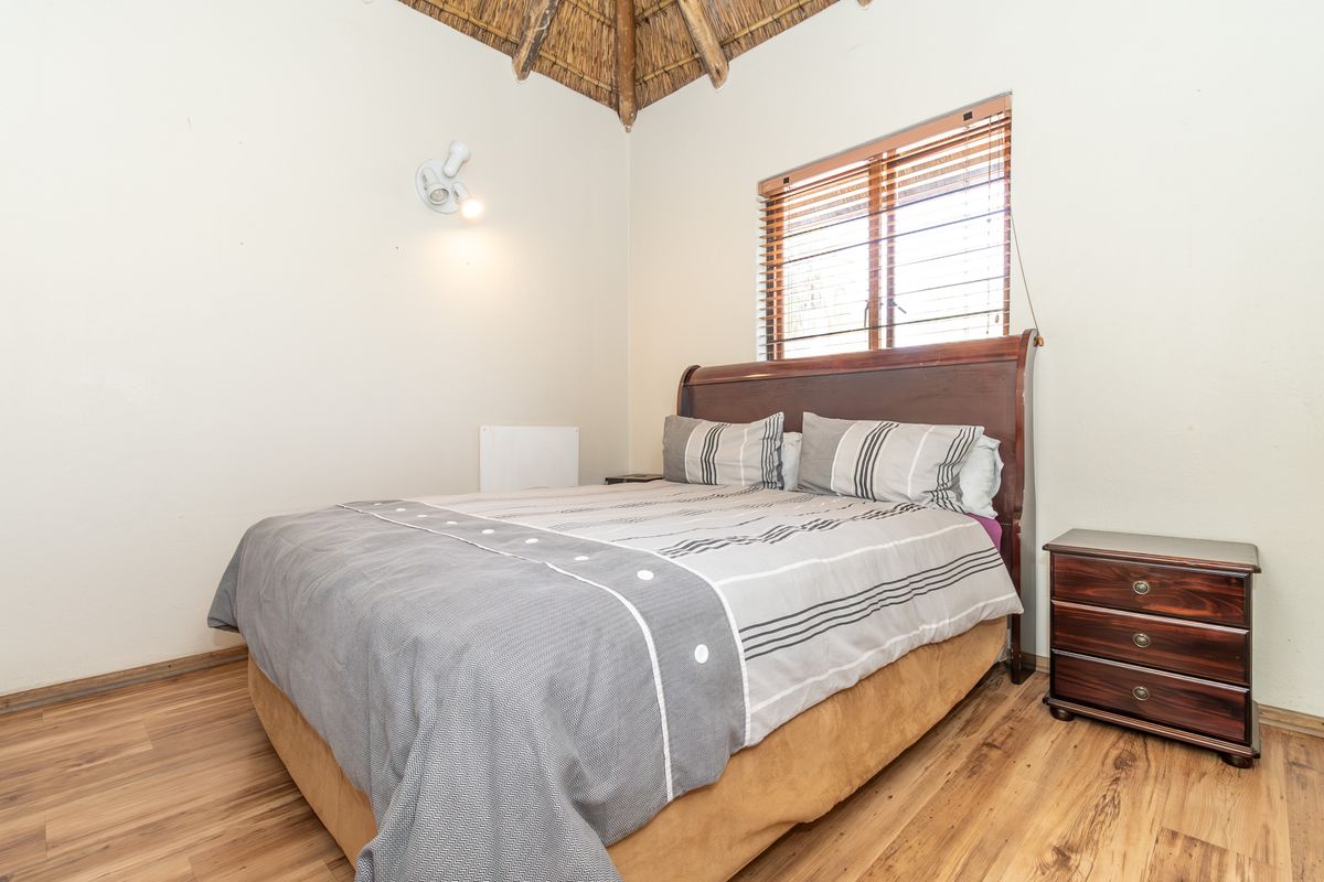 A cozy bedroom featuring a unique thatched ceiling, laminate flooring, and a window with fitted venetian blinds.