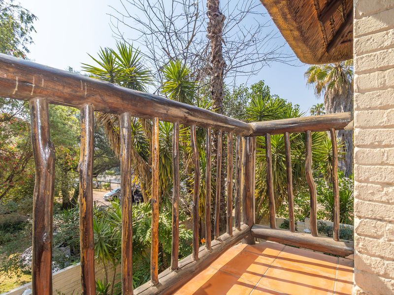 A rustic balcony featuring a timber railing, terracotta tiling, and a thatched roof overhang, overlooking a lush garden area.