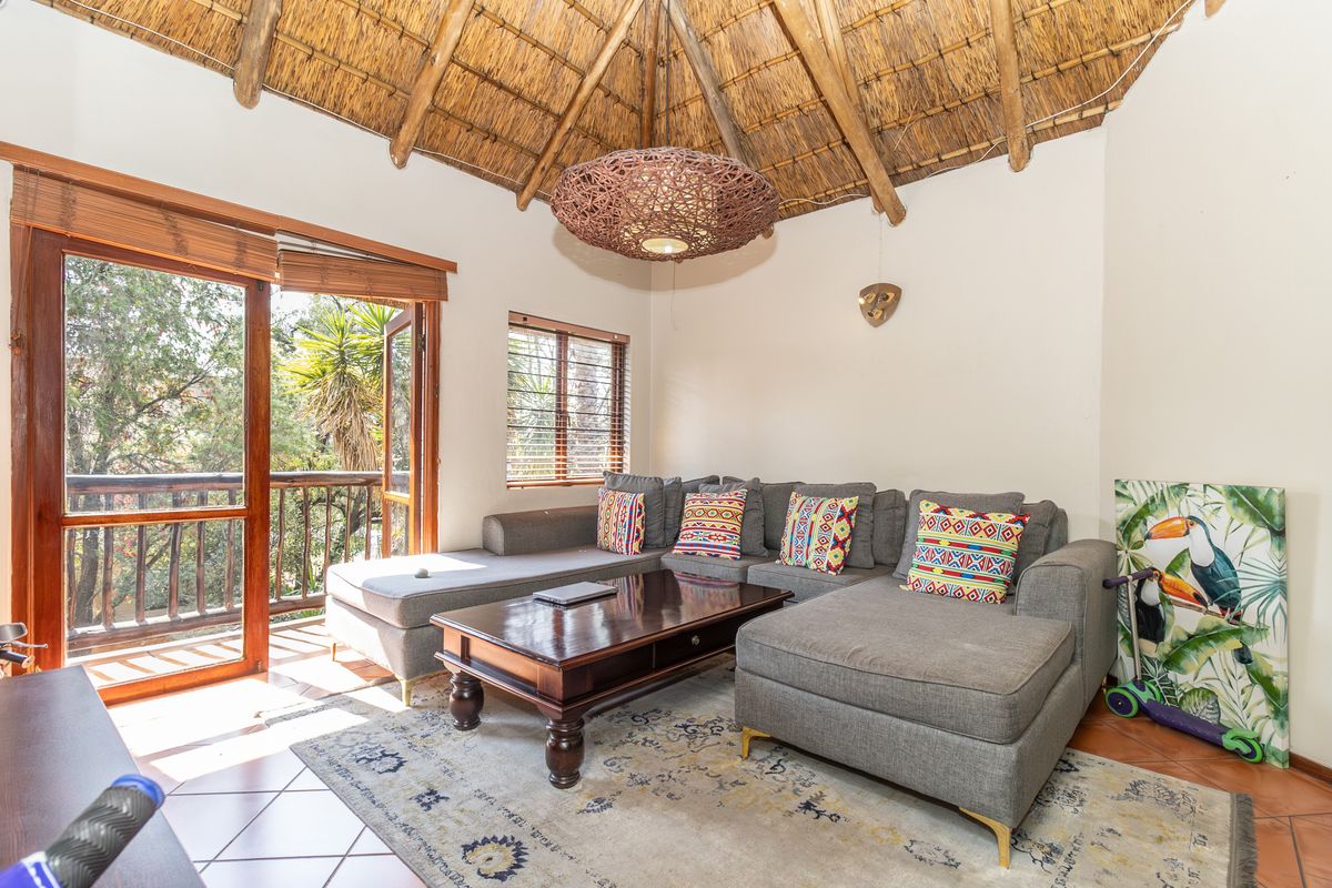 A cozy living room featuring a unique high thatched ceiling with exposed rafters, tiled floors, and direct access to a private balcony.