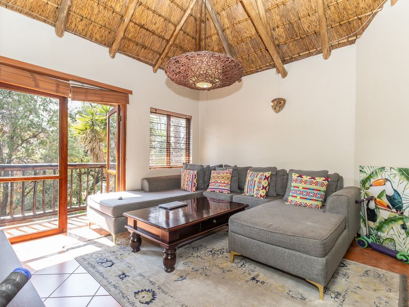A cozy living room featuring a unique high thatched ceiling with exposed rafters, tiled floors, and direct access to a private balcony.