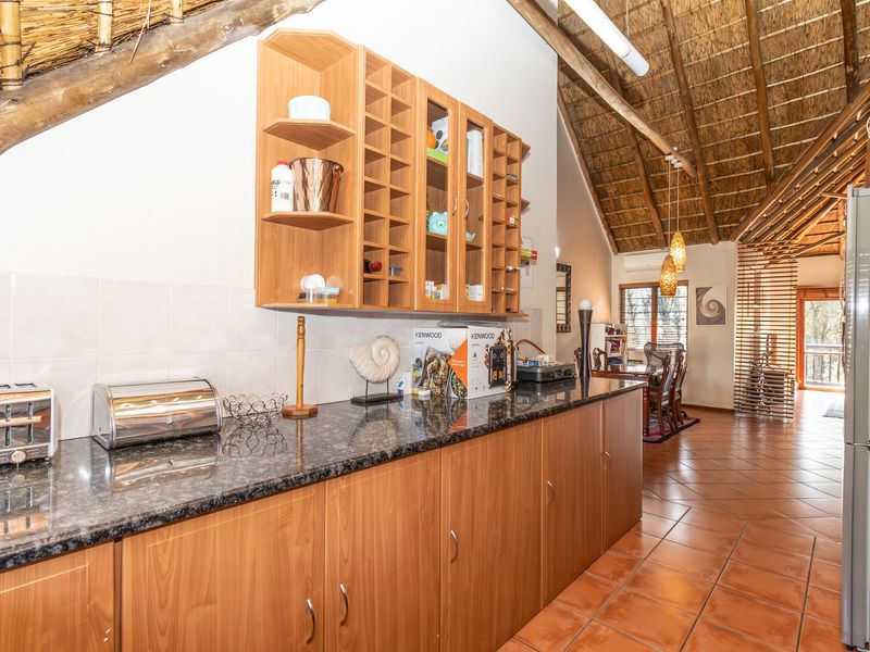 A kitchen area featuring granite countertops, laminate cabinetry, and a distinctive thatched roof with exposed timber beams, flowing into an open-plan living space.