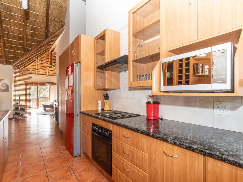 A functional kitchen featuring wood-finish cabinetry, granite countertops, integrated appliances, and a unique vaulted thatched ceiling, flowing into the open-plan living area.