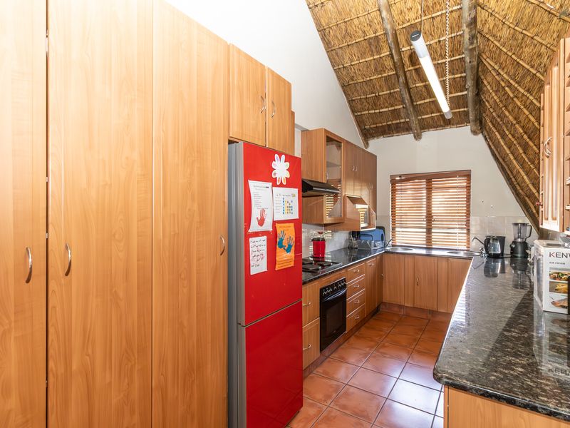 A functional kitchen featuring wood-finish cabinetry, granite countertops, built-in appliances, and a unique high-pitched thatched ceiling with exposed timber rafters.