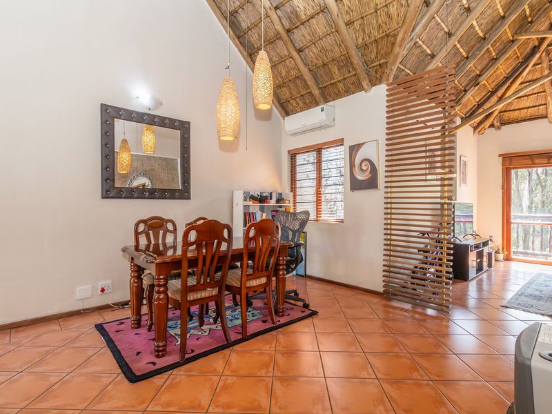 Open-plan living and dining area featuring a high vaulted thatched ceiling with exposed timber rafters and terracotta floor tiles.
