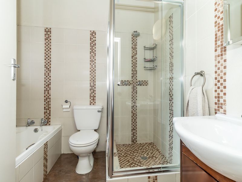 A functional bathroom featuring a separate shower enclosure, bathtub, toilet, and vanity basin with decorative tiled accents.