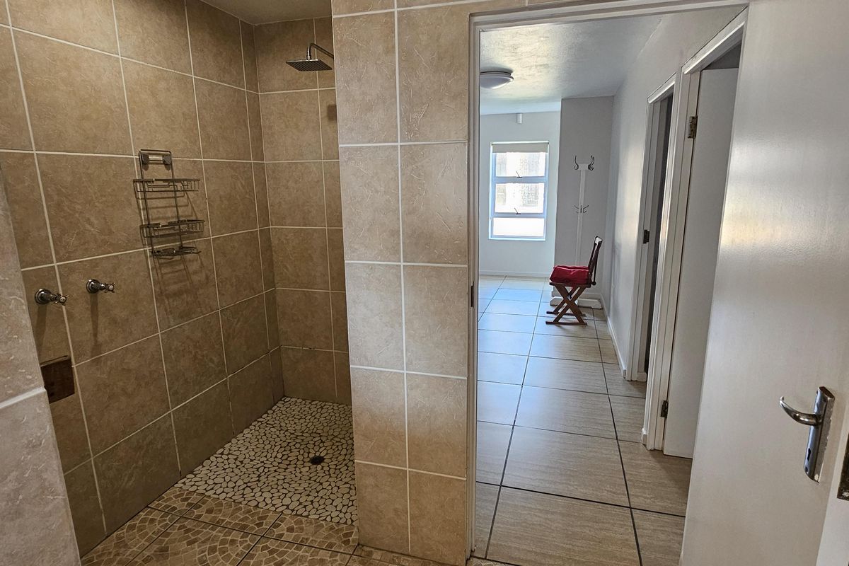A bathroom featuring a walk-in shower with pebble-style flooring and neutral wall tiling, leading into a tiled hallway.