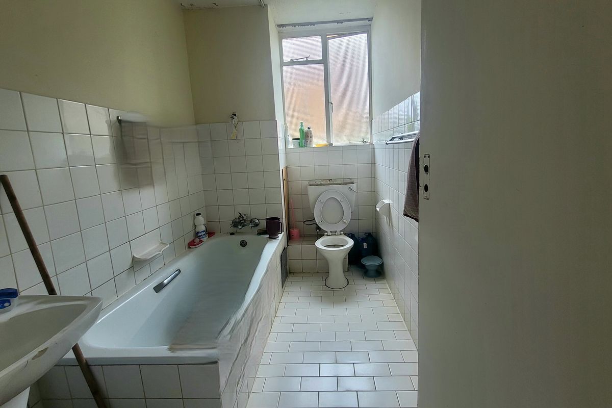A dated bathroom featuring a standard bathtub, toilet, and basin with tiled finishes and an obscured glass window.