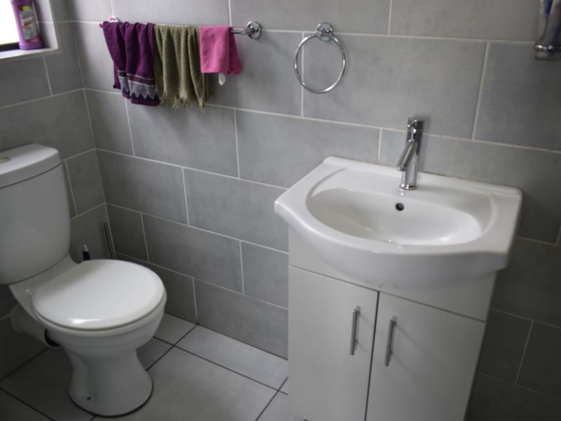 A compact bathroom featuring grey wall tiles, a white vanity cabinet with a basin, and a standard toilet.