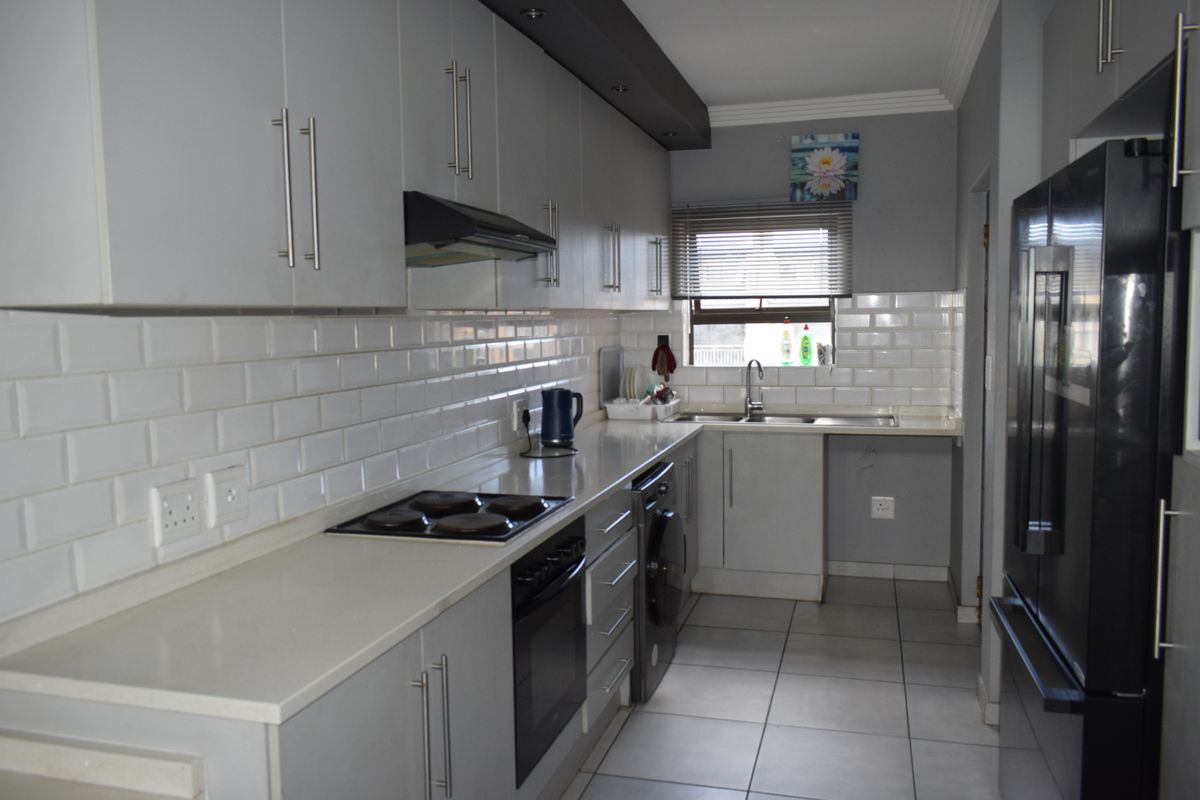 Modern galley-style kitchen featuring grey cabinetry, subway tile backsplash, integrated oven and hob, and tiled flooring.
