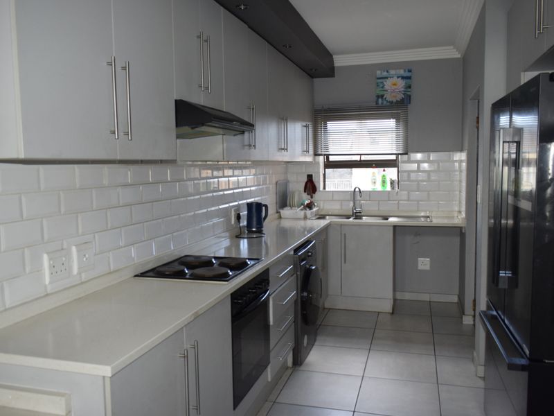 Modern galley-style kitchen featuring grey cabinetry, subway tile backsplash, integrated oven and hob, and tiled flooring.