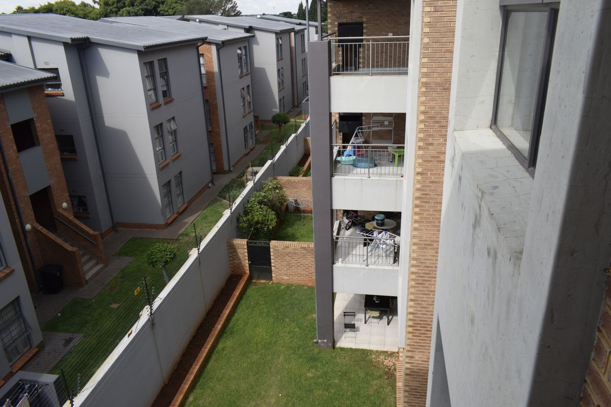 An elevated view of the townhouse complex rear exterior, featuring stacked balconies, private garden spaces, and perimeter security fencing.